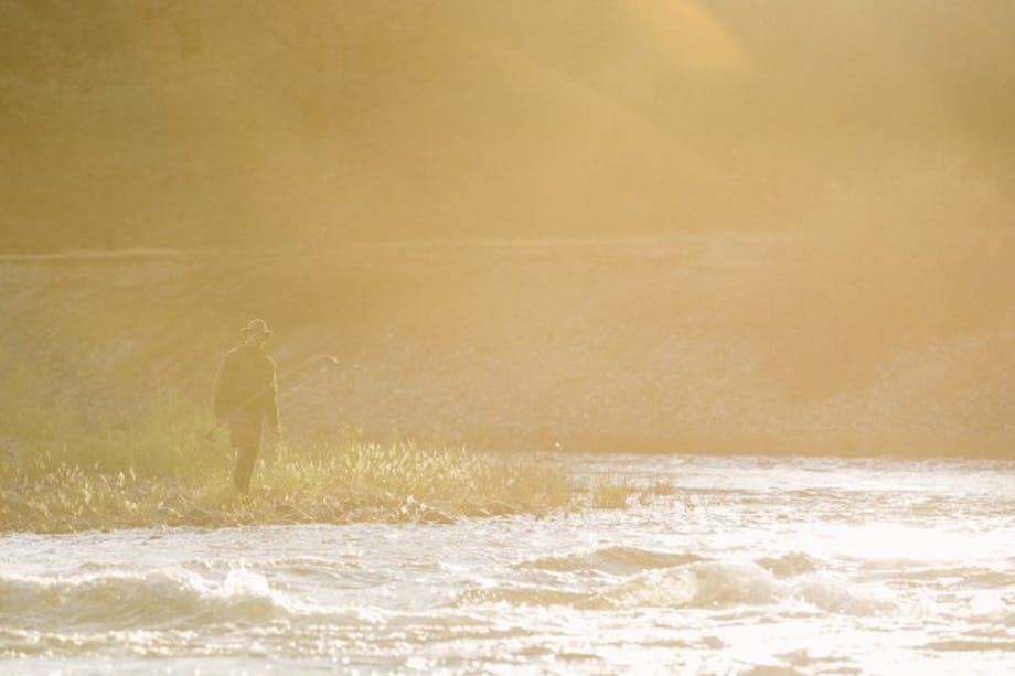 sunburst silhouette of man approaching river holding flyfishing rod