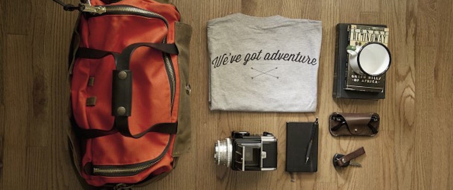 Packing setup on wooden floor duffel, shirt journal camera glasses and book