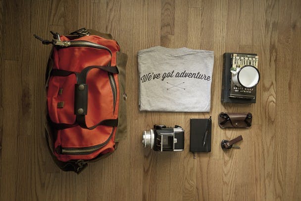Packing setup on wooden floor duffel, shirt journal camera glasses and book
