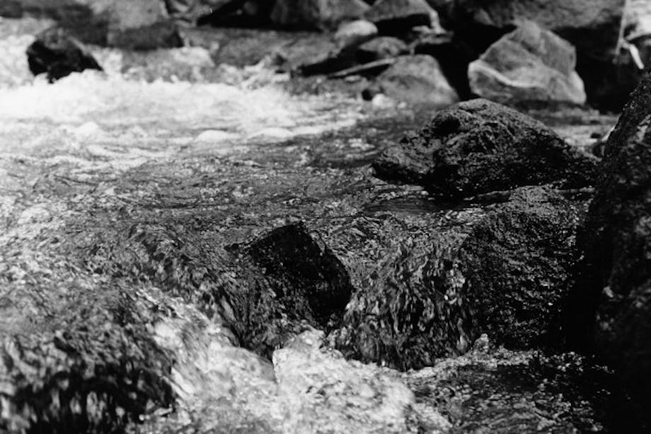 man stands upriver in rushing water among large rocks