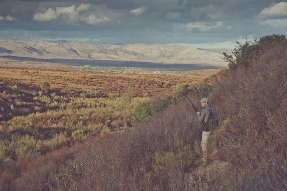 hunter with pack surveys sage-brush valley from hilltop