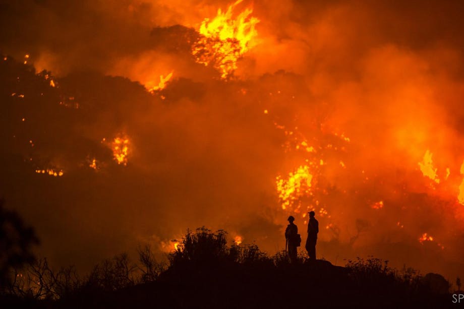 two firefighters silhouetted by raging fire in background