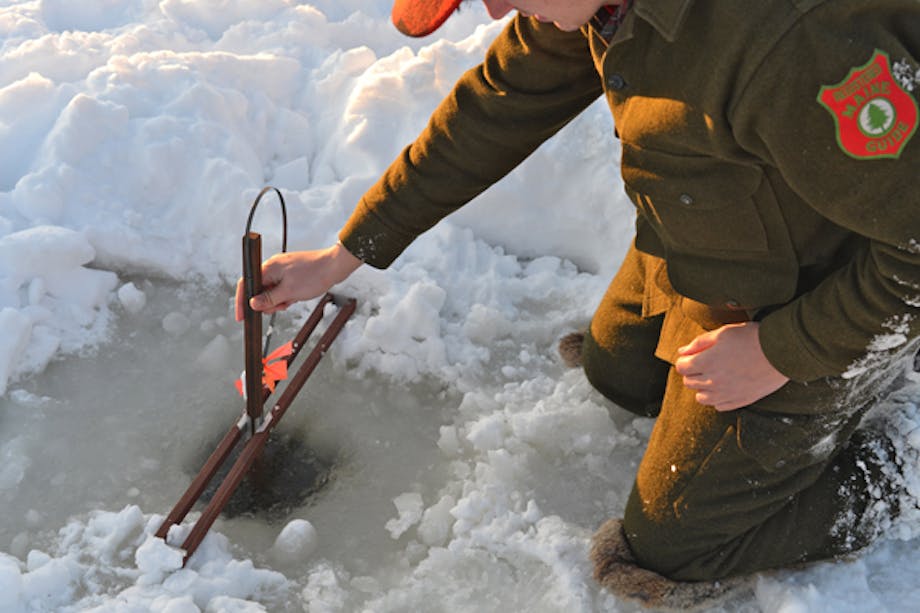 Ice Fishing - Man in olive wool coat and pants sets up ice fishing hole