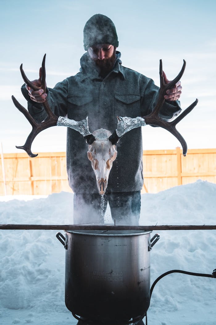person in snowy yard lowering elk skull with antlers into steaming pot