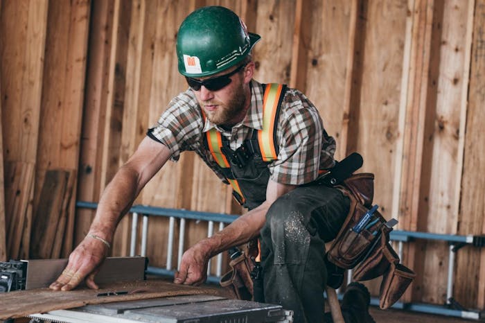 carpentry worker rips board in shortsleeve plaid shirt and hardhat