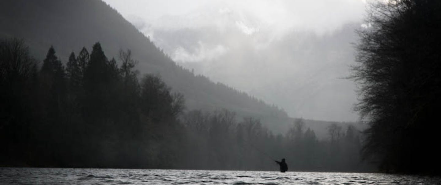 fly fisherman in river with alpine lined mountain ridge backdrop