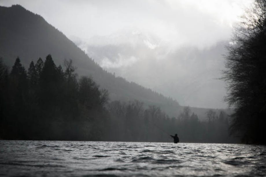 fly fisherman in river with alpine lined mountain ridge backdrop