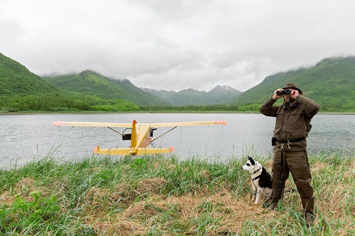karelian bear dog and master stand in front of yellow seaplane in lake