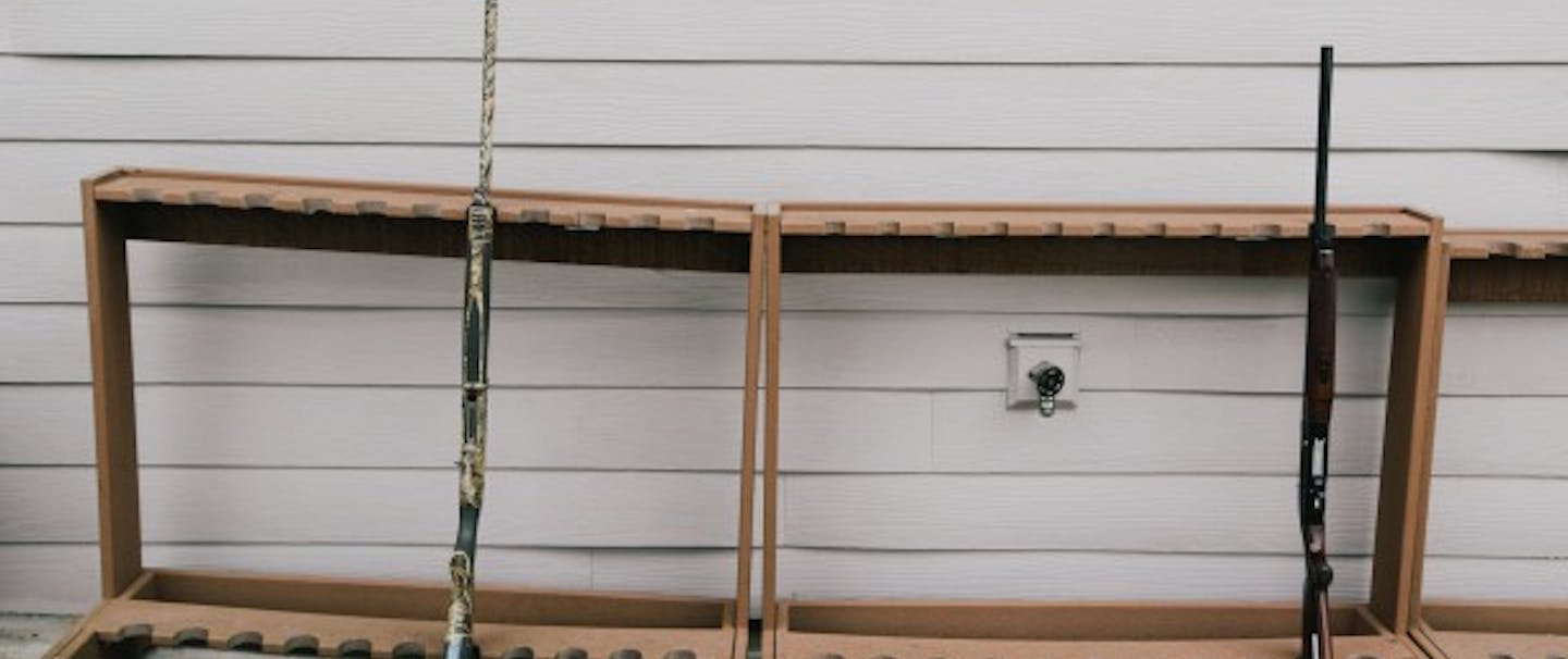 gun rack with two shotguns in front of wall with vinyl siding
