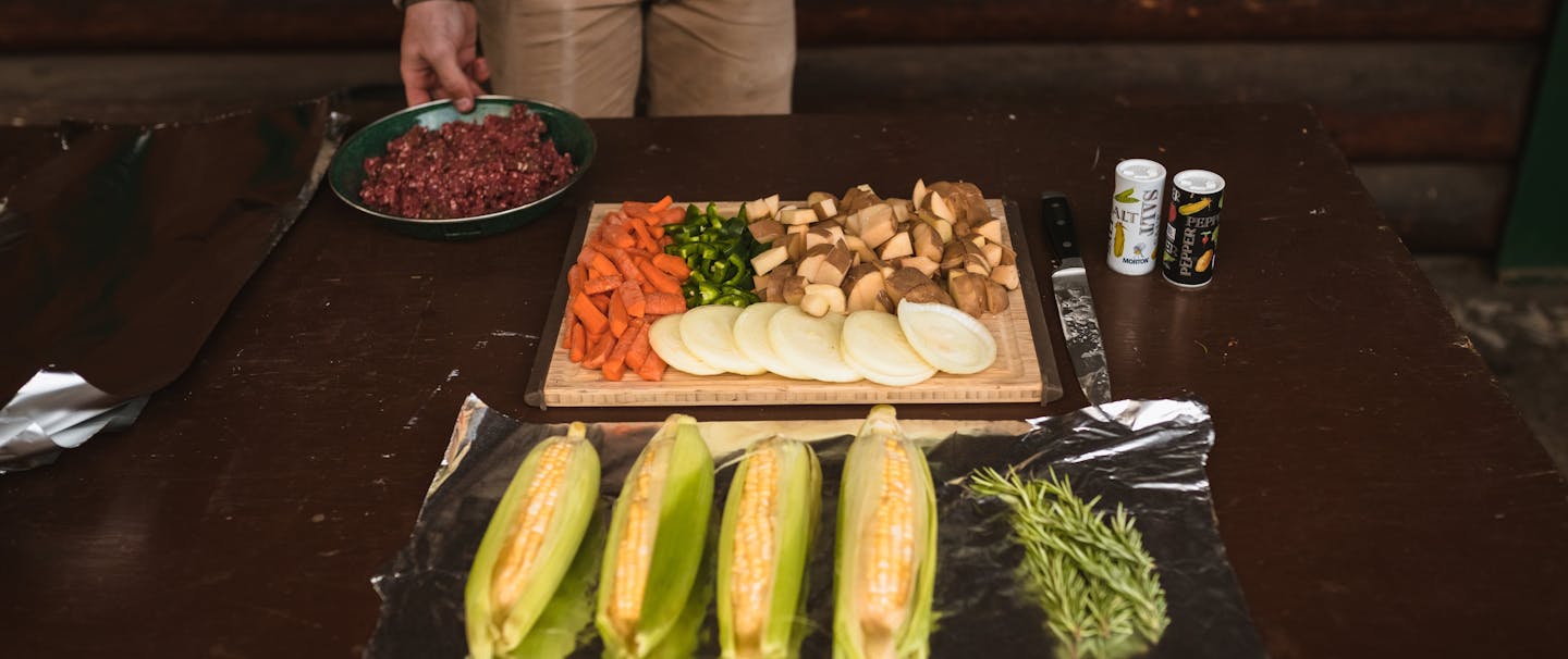 man prepping meal of veggies, corn, herbs, and meat at prep table
