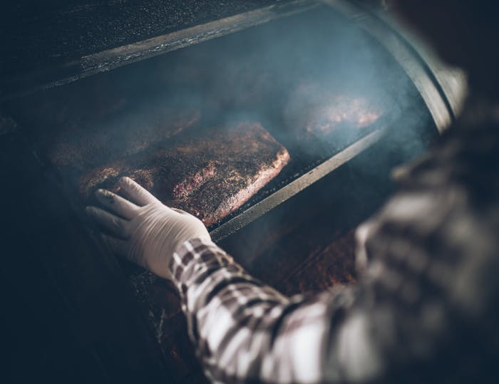 gloved hand touches meat in smoker