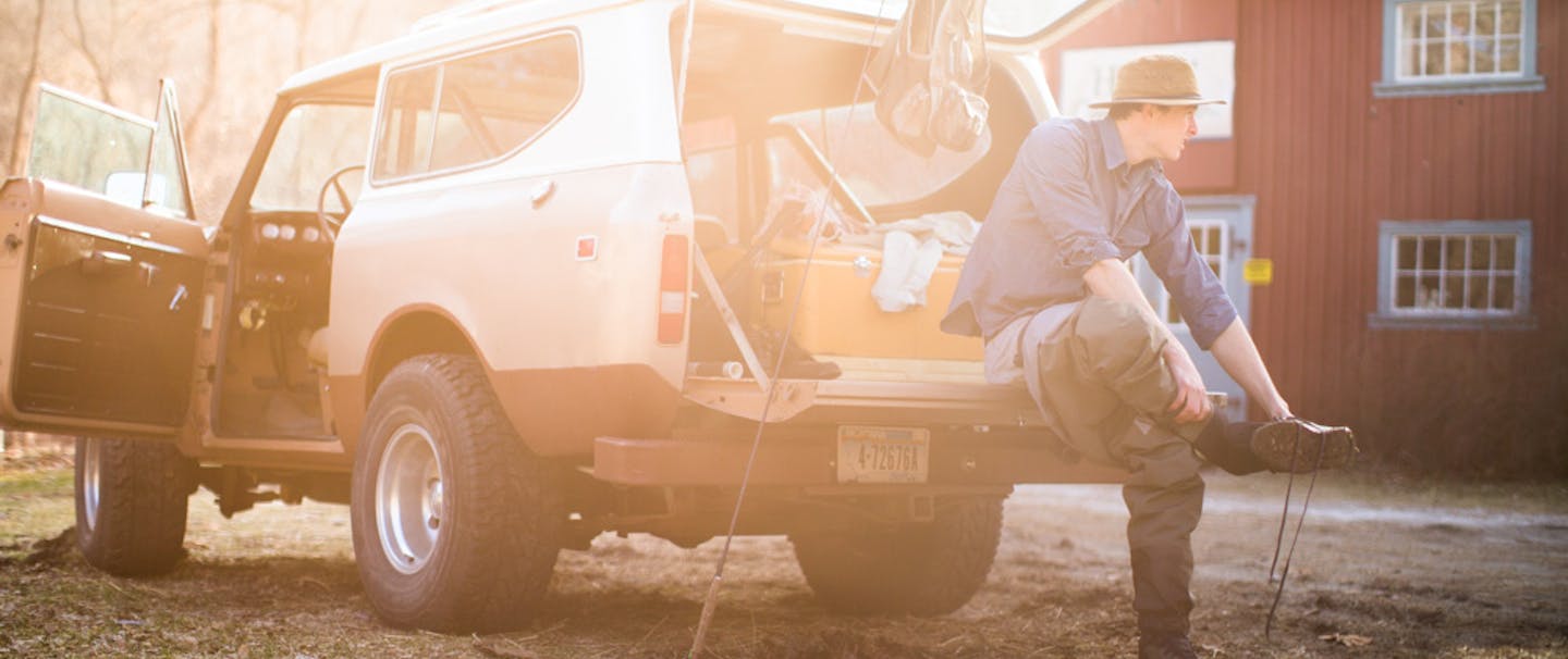 man removes waders and boots after flyfishing sitting on tailgate of his bronco