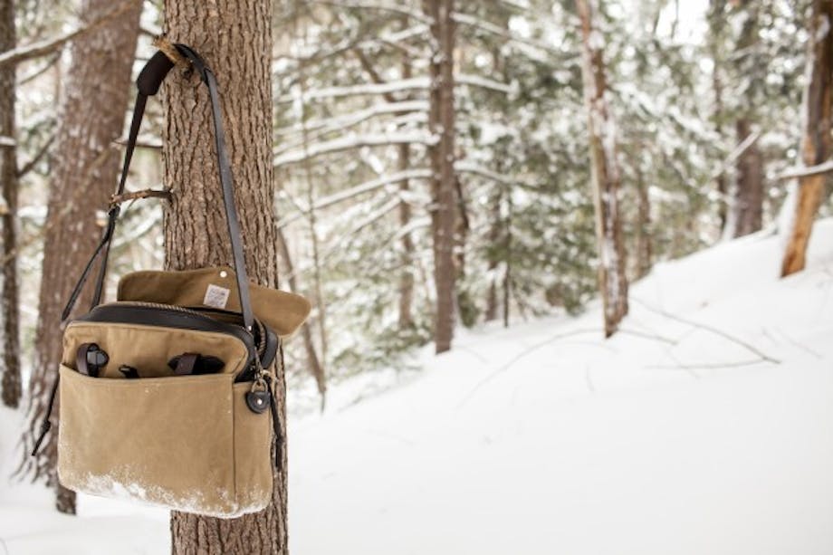 Beige filson bag hangs on a tree branch in snowy forest