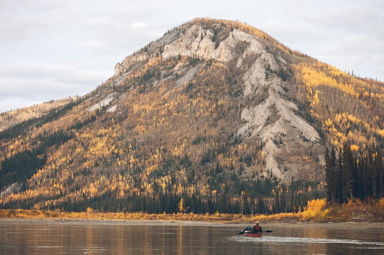 man in a canoe on the Yukon river, a large mountain in the distance