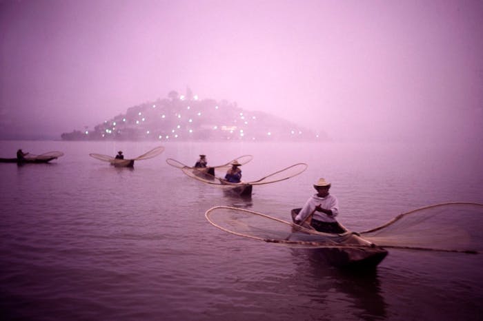curving line of fishermen with single man boats and fishing nets in front of lighted island