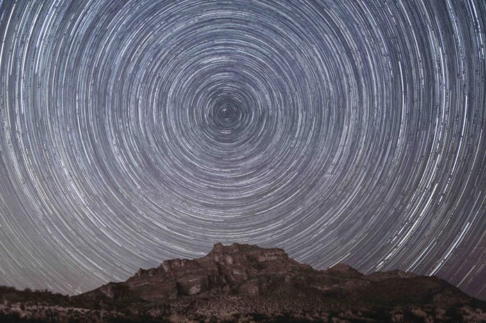 long exposure shot of circular star trails above rocky mountain