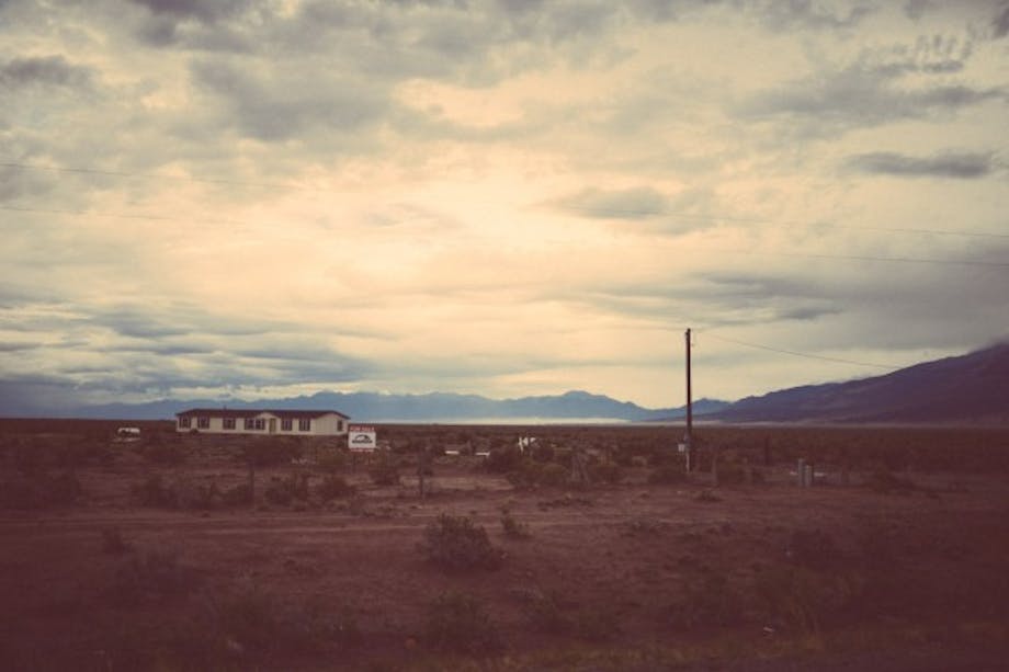 house in desolate desert landscape with large mountains in background and big open sky