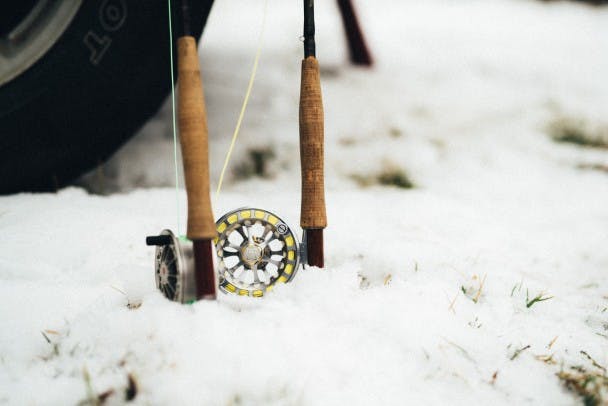 two fly fishing rods and spools protruding out of snow