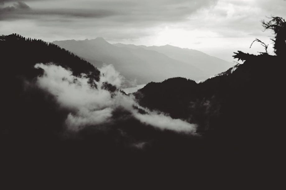 Black and white alpine hills and clouds with river and mountains in background