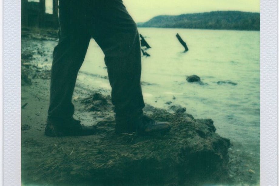 polaroid of man standing at edge of large body of water