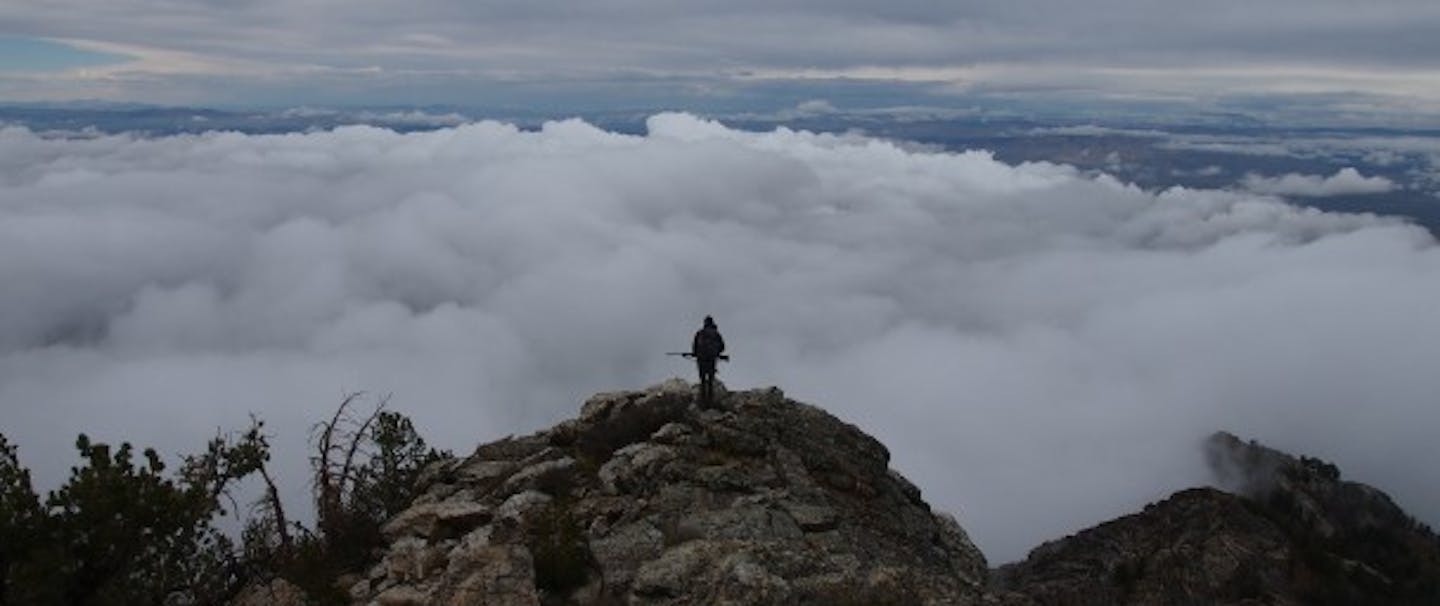 Snowcock Hunting; hunter stands on mountaintop above the clouds
