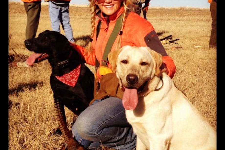 Female hunter poses with black and yellow lab in high-vis gear