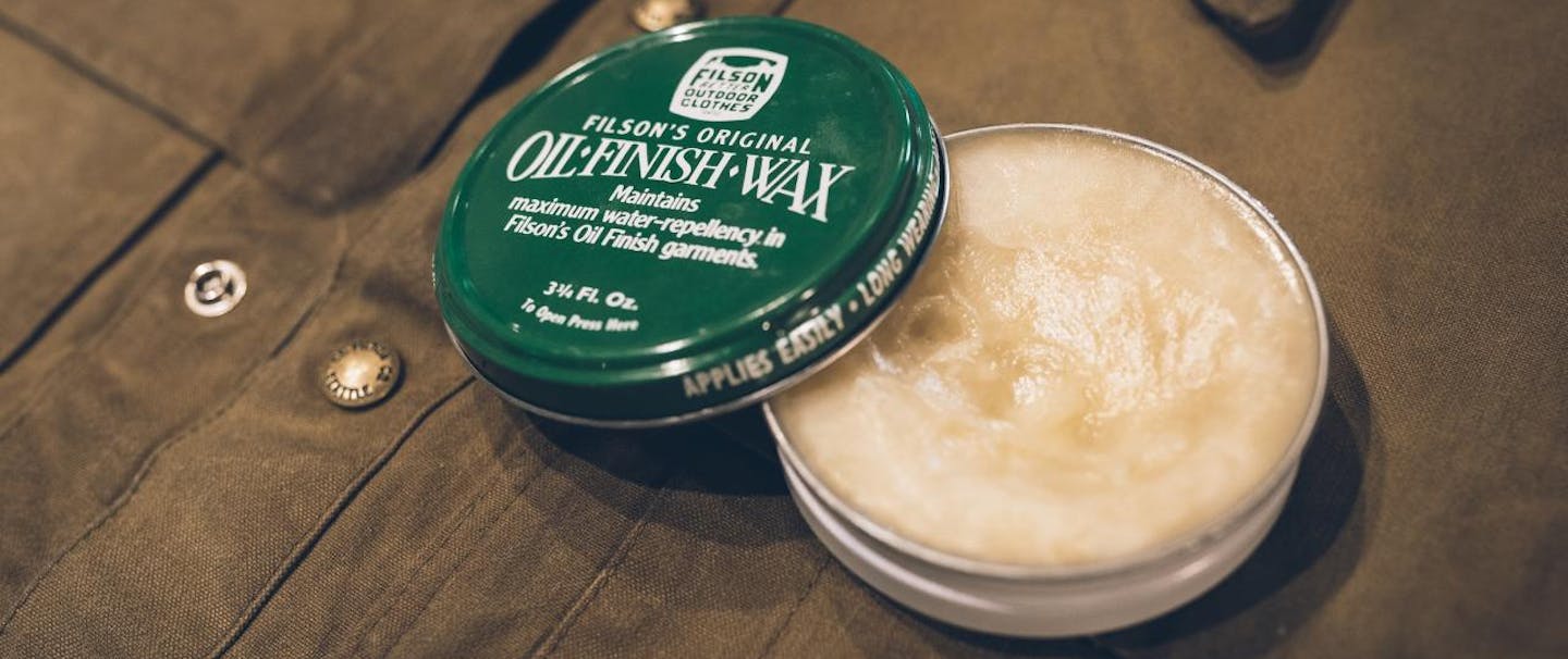 green tin of filson oil finish wax sits on top of brown jacket