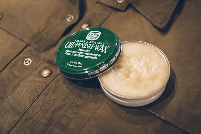 green tin of filson oil finish wax sits on top of brown jacket
