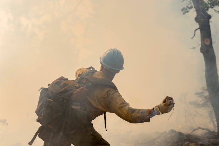 wildland firefighter throwing retardant in smoky forest