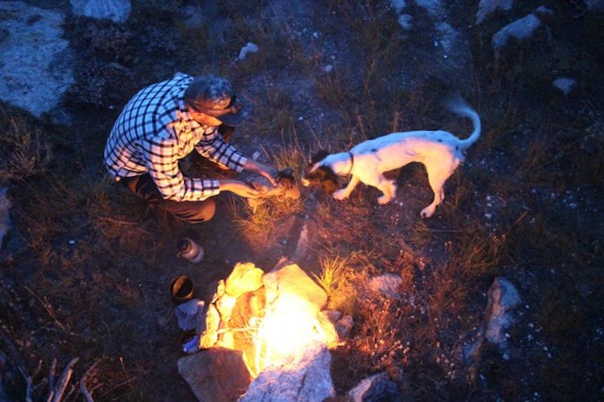 man prepping bird to cook over campfire with dog