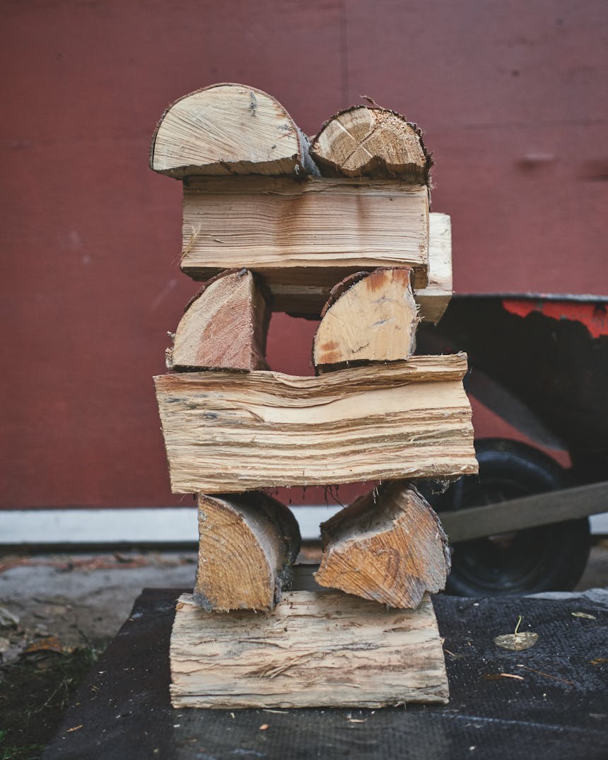 a stack of firewood with two pieces going one direction, while the next two are in the opposite direction, six pieces high with a red wheelbarrow and building behind it