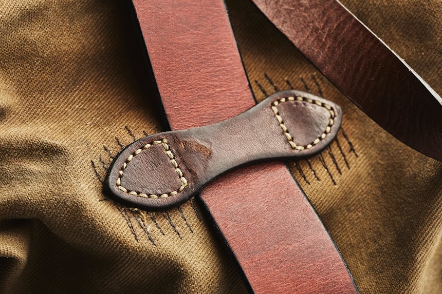 a close up image of a worn tan duffle bag with old and leather handles, and extra stitching where it needed to be mended for the leather handles