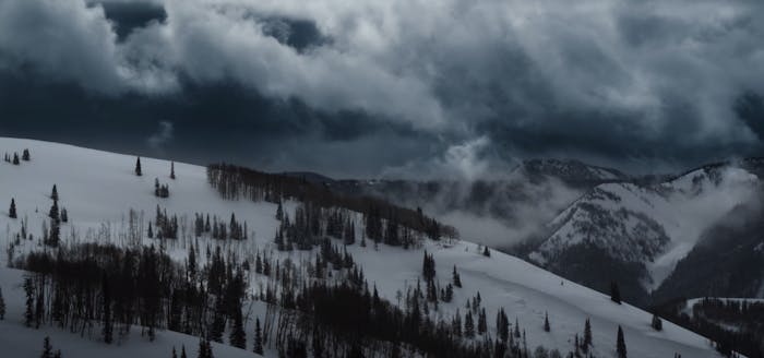 a snowy dark landscape of the Utah mountains with patches of trees and a storm rolls in