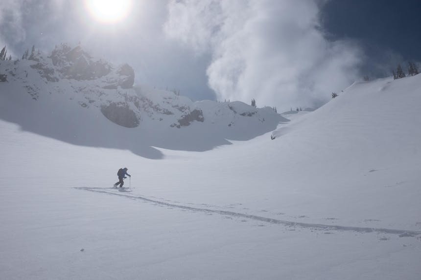 skier skiing up an incline to the top of a peak with the sun shining down