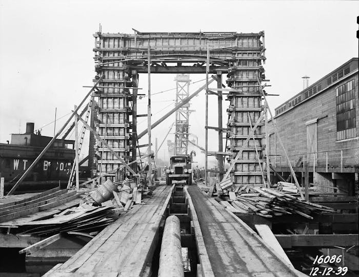 a straight on view of the work in progress build of the ballard bridge as an old car drives towards the cameraman