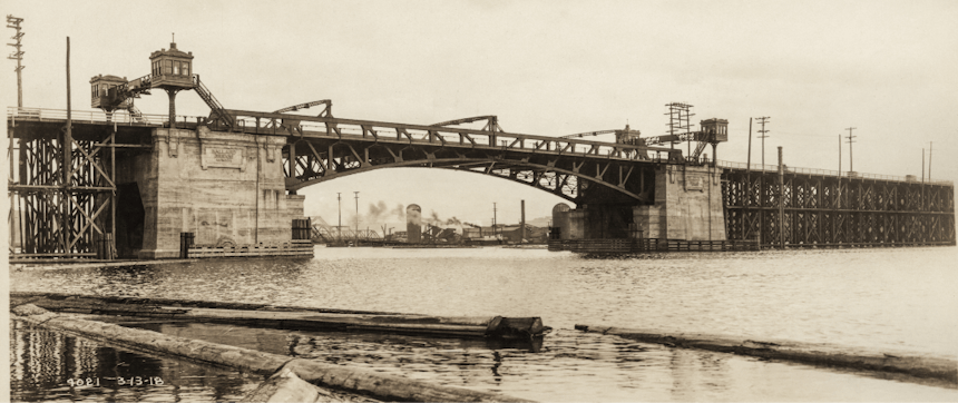 an old sepia colored image from the river bank looking up towards the ballard bridge build