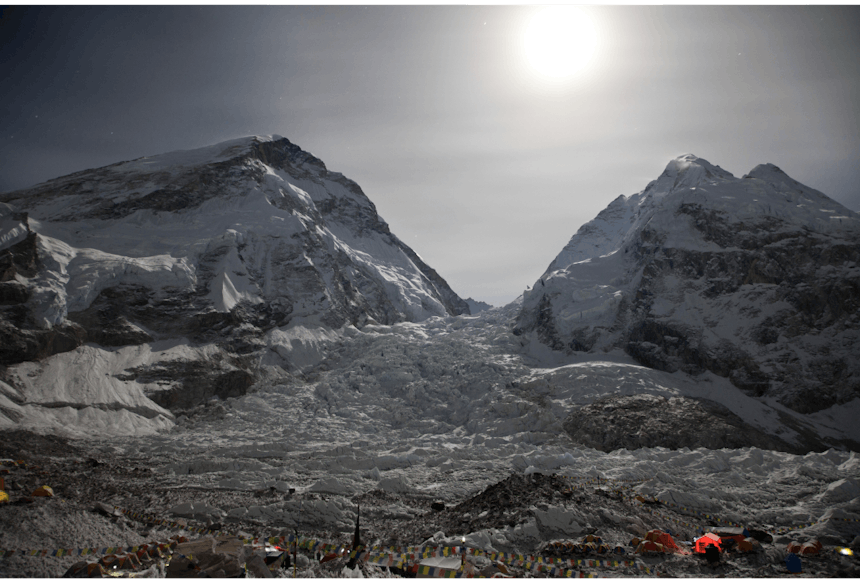 a landscape shot looking at two mountain peaks with a valley between them and the sun high in the cloudy sky