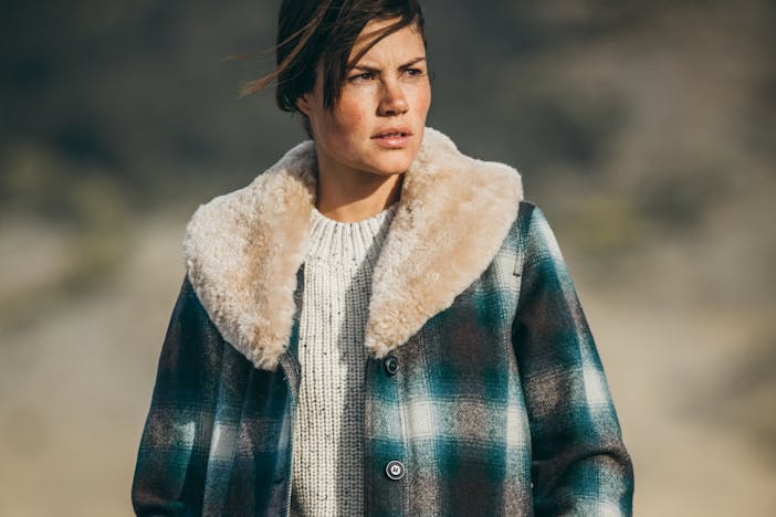 a brunette woman wearing a cream wool sweater under a blue, black and white plaid coat with a wool collar looking off to the right