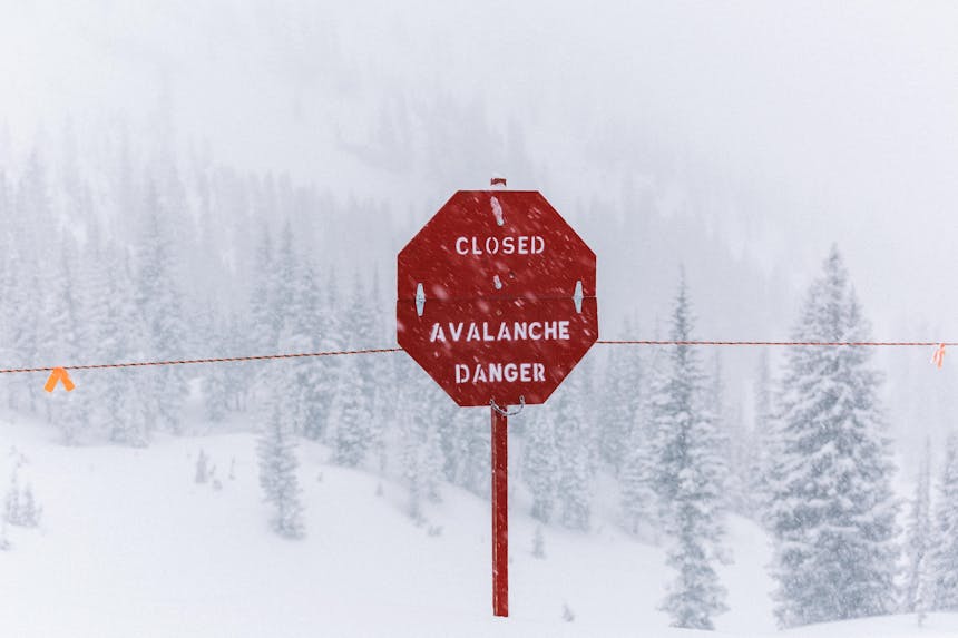a red stop sign with words CLOSED AVALANCHE DANGER along the edge of a drop off