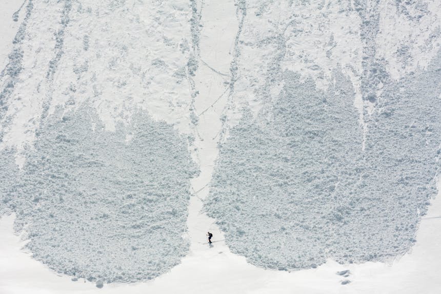 a aerial shot of a skier in the middle of two avalanches coming down the mountain and nearly coming together trapping them