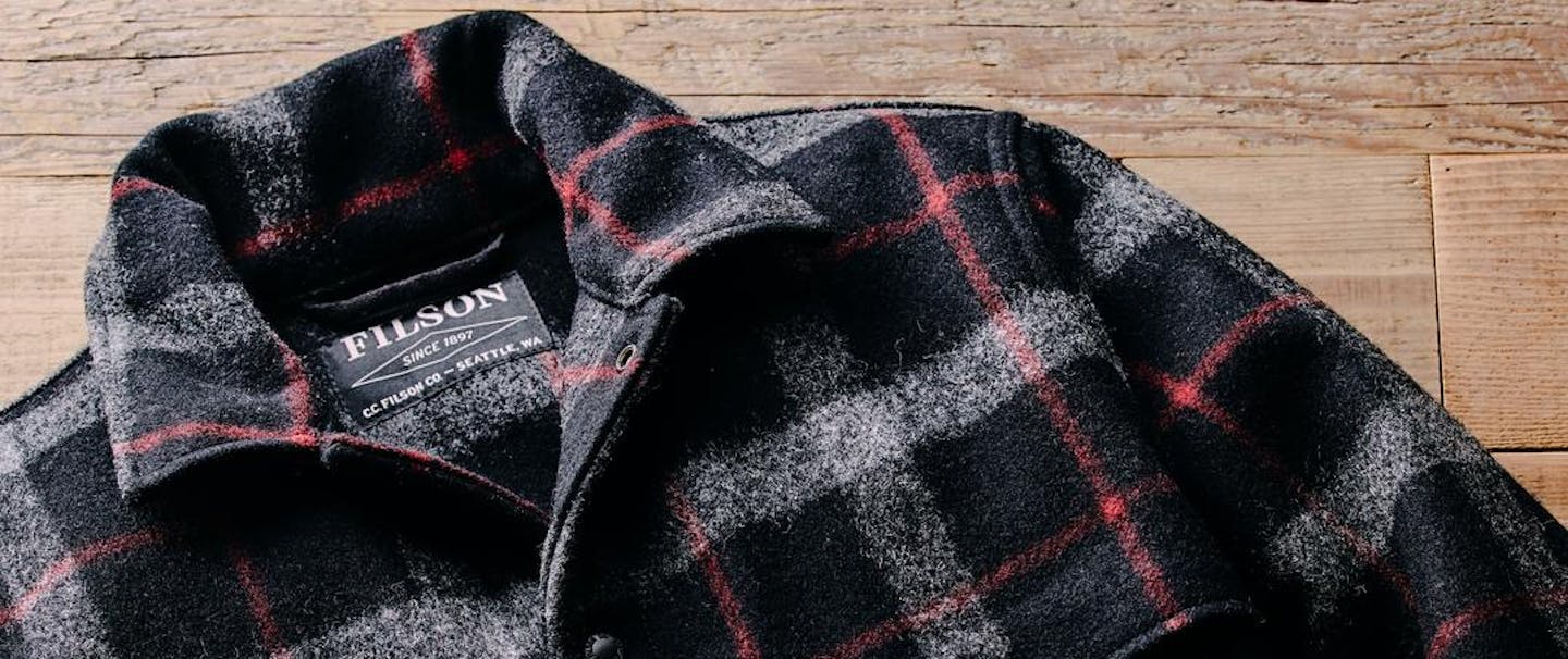 a lay down of a black, white and red flannel pattern Filson Mackinaw Wool Cape Coat on rustic wood