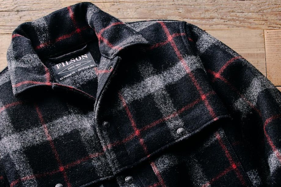 a lay down of a black, white and red flannel pattern Filson Mackinaw Wool Cape Coat on rustic wood