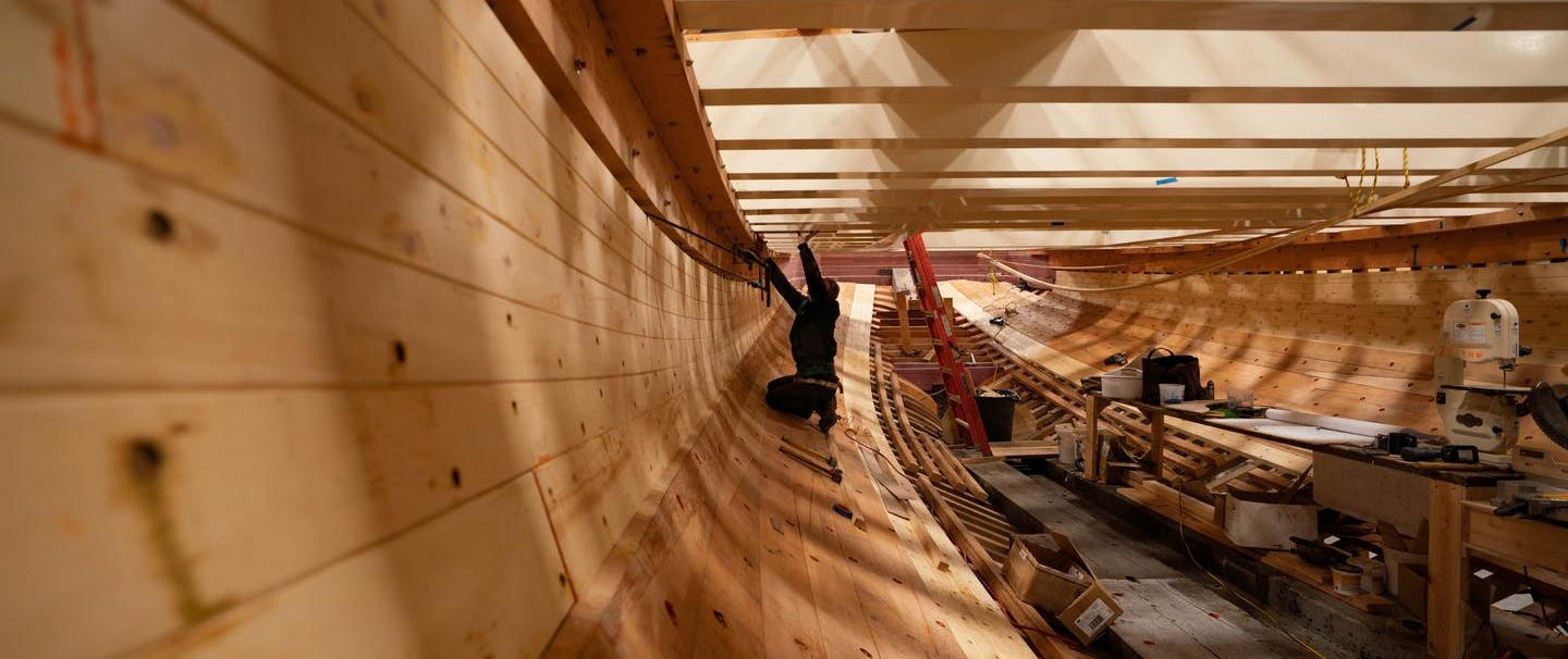 man working under the deck of a wooden ship being built