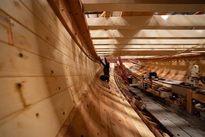 man working under the deck of a wooden ship being built