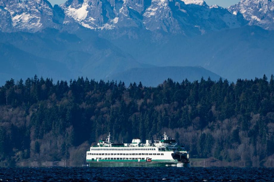 image from afar capturing the landscape of a Puget Sound ferry crossing the water with mountains towering overhead