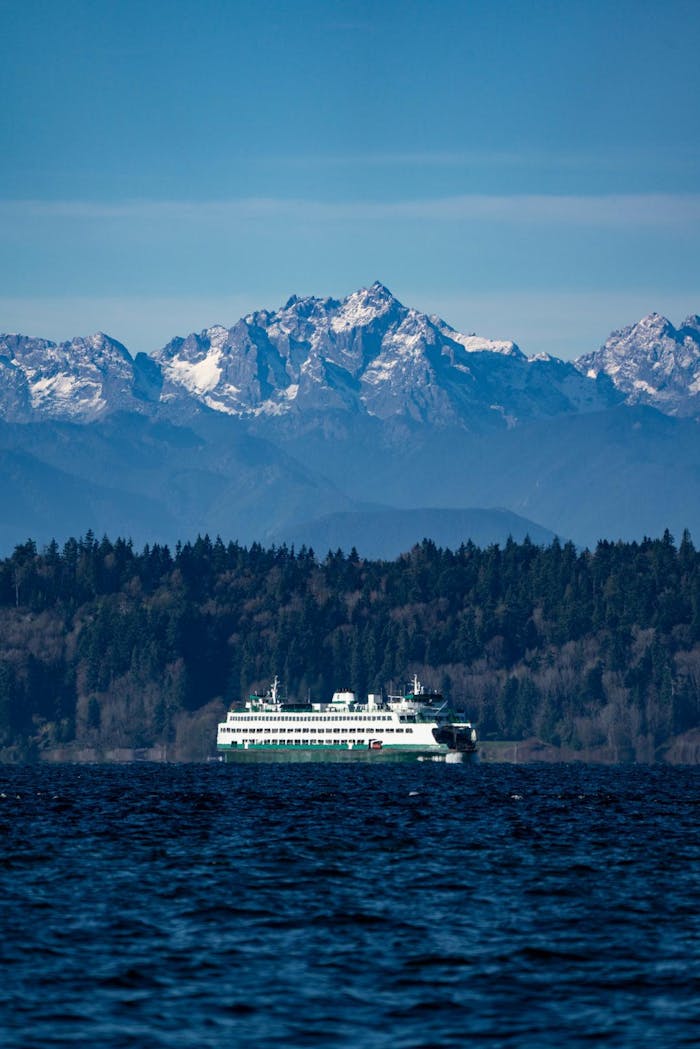 image from afar capturing the landscape of a Puget Sound ferry crossing the water with mountains towering overhead