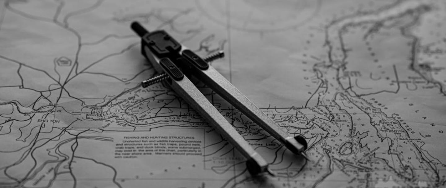 a black and white top down view of a nautical chart with a compass laying on top