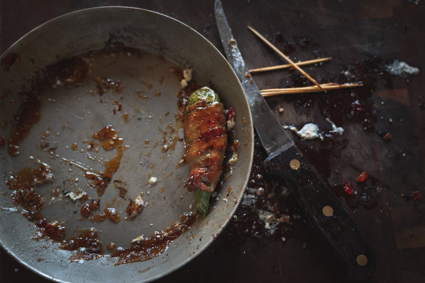 the last fire roasted jalapeno popper wrapped in bacon left in a metal bowl with a knife and toothpicks on the side