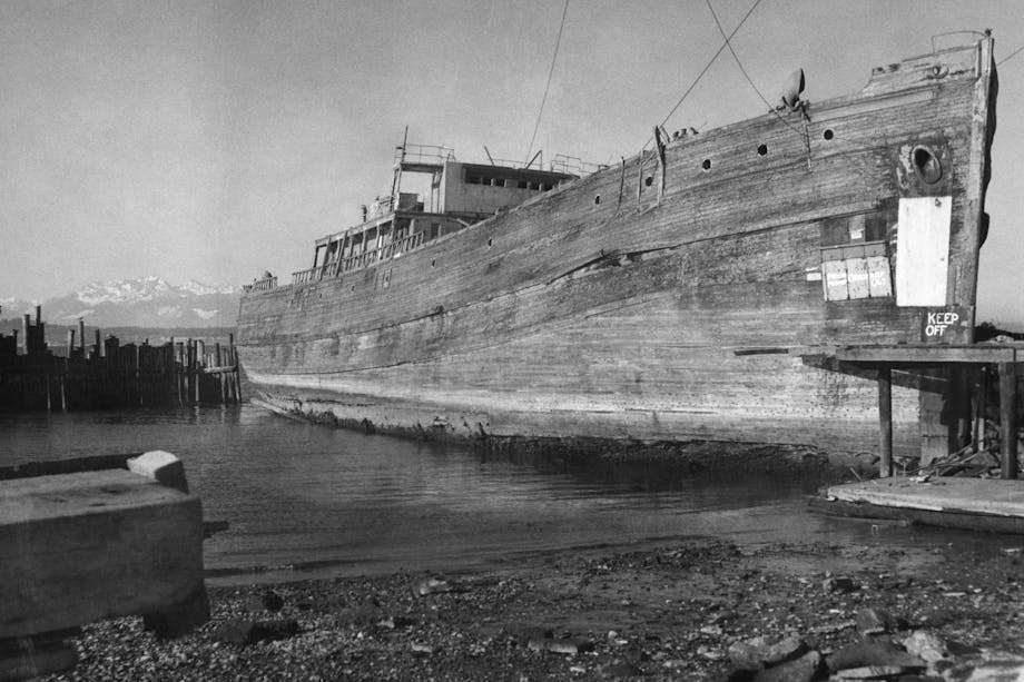 large derelict wooden ship docked on a black sandy/muddy beach