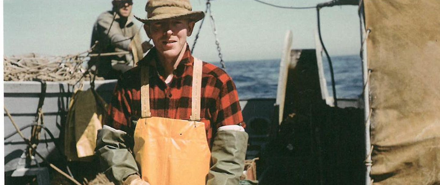 man on boat in red plaid shirt and tan apron prepares a halibut stomach as bait on a wooden surface